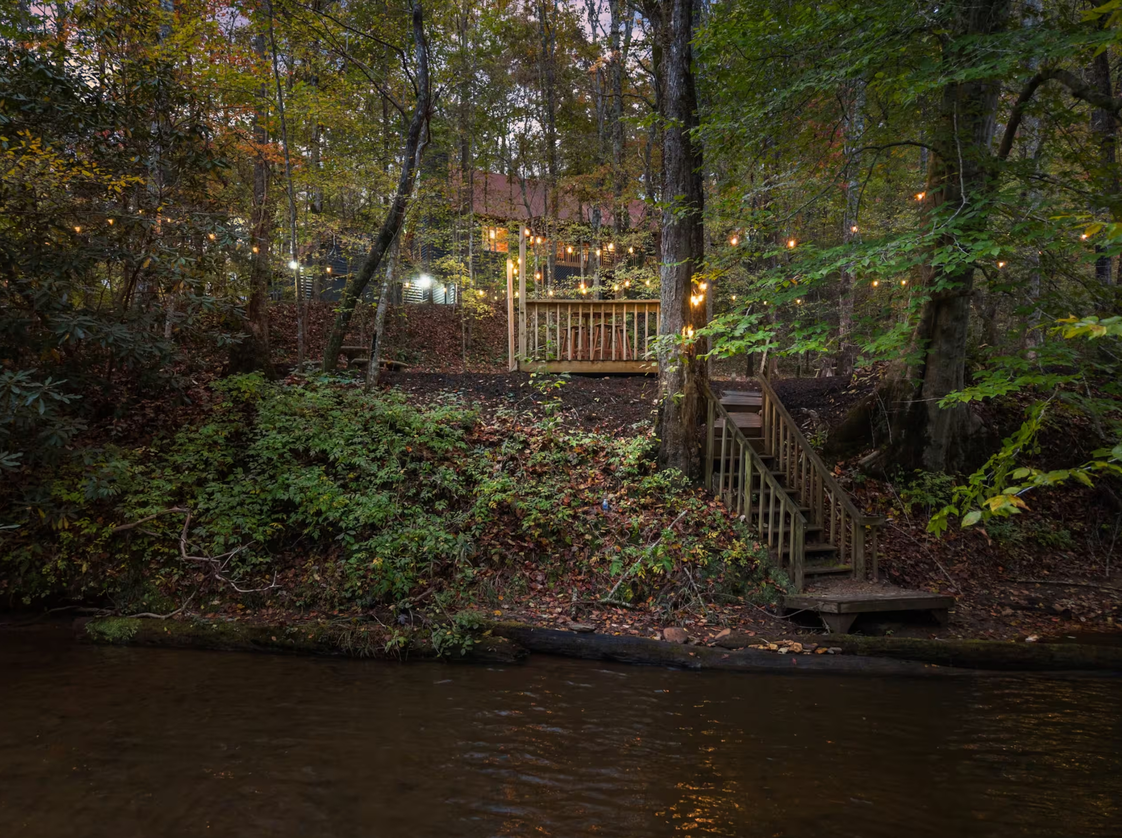 View of the cabin from the river at dusk with string lights